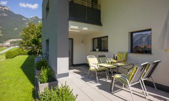 A cozy balcony with a table and chairs. The surroundings are green and offer a view of the mountains.