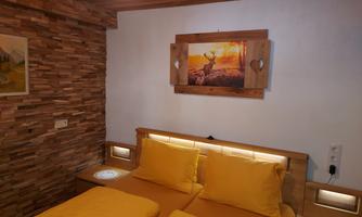 A cozy bedroom with wooden paneling and a large window. The beds are covered with yellow bedding and a picture of a deer hangs on the wall.