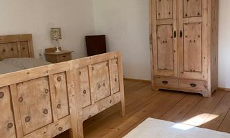 A bright bedroom with wooden furniture. There is a bed, a nightstand, and a wooden wardrobe.