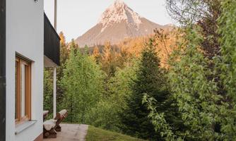 A beautiful view of a mountain, surrounded by trees. In the foreground, there is a terrace area of a house.
