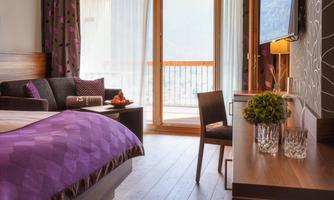 A modern hotel room with a cozy bed and elegant furniture. Large windows provide plenty of light and a view of the terrace.