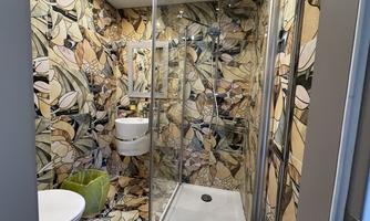 A modern bathroom with colorful, floral wall design. It includes a shower, a toilet, and a small green waste bin.
