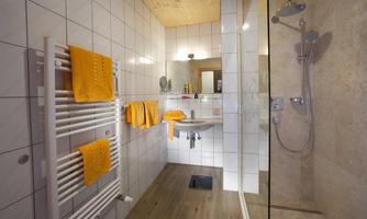 A modern bathroom with bright tiles and a glass shower. Towels in vibrant orange add a fresh accent to the space.