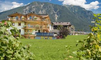 A picturesque landscape with houses near a green field. In the background, majestic mountains rise under a clear sky.
