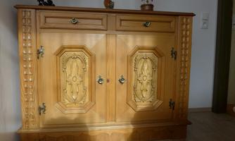 An antique wooden cabinet with intricate decorations and two doors. The piece of furniture is located in a bright room with a wooden floor.