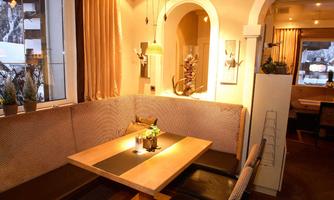 A cozy restaurant with stylish interior. There is a wooden table with elegant seating and soft lighting.