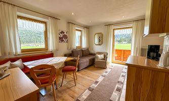 A cozy living room with a dining area and a couch. The large windows offer a view of the nature outside.