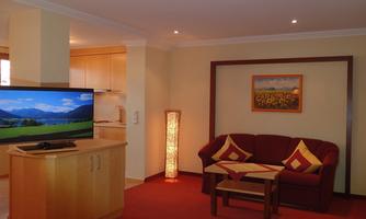 A cozy living room with a red couch and a television. On the wall hangs a picture of sunflowers.