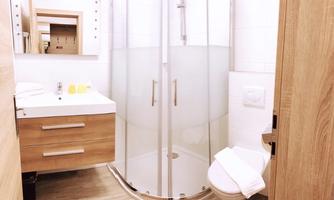 A modern bathroom with a shower cabin and a sink. The furniture is made of light wood and the walls are tiled in white.