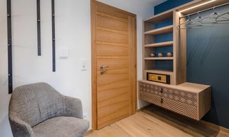 A modern entrance area with a wooden cabinet and a cozy gray seating area. The wall is painted dark blue and there is a wooden ceiling.