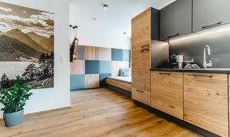 A modern kitchen with wooden elements and a cozy living area. A landscape painting hangs on the wall, reflecting the surroundings.