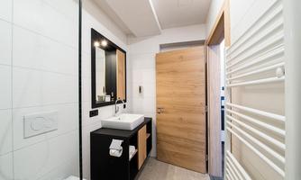 A modern bathroom with a black vanity combo and a large mirror. The walls are light-tiled and the door is made of wood.