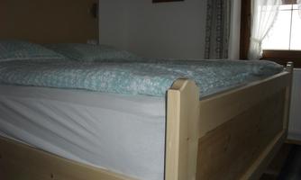 A large bed with light blue bedding in a quiet room.  
Daylight spills through the window, creating an inviting atmosphere.