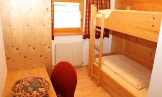 A cozy room with a wooden bunk bed. There is a desk and large windows that let in plenty of daylight.