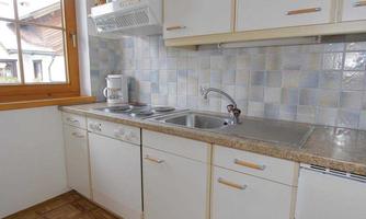 A modern kitchen with white cabinets and a bright countertop. It features a sink, stove, and windows with natural light.