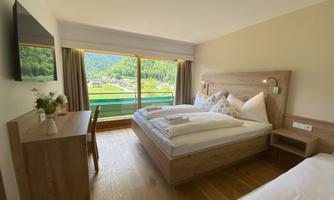 A modern bedroom with two beds and a large window. The view looks out onto a green landscape and gentle hills.