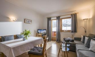 A bright living room with a dining area and a couch. Large windows let in plenty of light and offer a view outside.