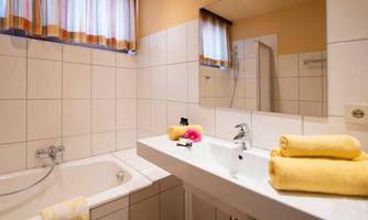 A modern bathroom with a bathtub and a sink. Yellow towels and a flower give the room a friendly atmosphere.