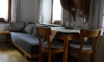 A cozy living area with a couch and a small dining table. The windows let in a lot of light and create an inviting atmosphere.