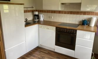A modern kitchen corner with white cabinets and a wooden countertop. The equipment includes a stove, dishwasher, and coffee machine.