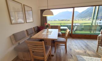 An inviting dining area with a table and chairs, surrounded by large windows overlooking the mountains. The warm wood tones and cozy decor create a pleasant atmosphere.