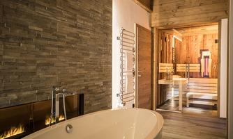 A modern bathroom with a freestanding bathtub and a sauna in the background. The walls are made of natural stone and wood, creating a relaxing atmosphere.