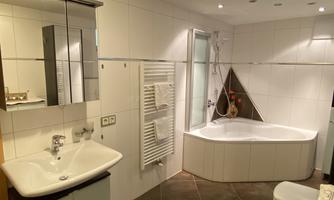A modern bathroom with a bathtub, a sink, and a large mirror. The walls are brightly tiled, and the lighting creates a pleasant atmosphere.