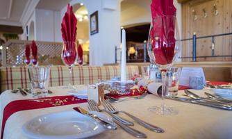 An elegantly set table in a restaurant with red napkins and glasses. There is cutlery and plates carefully arranged on the table.