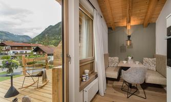 A cozy living space with a wooden ceiling and modern design. Through the open window, one looks out at a picturesque mountain landscape.