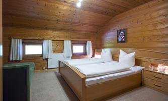 A cozy bedroom with wooden paneling and two windows. The bed is decorated with white pillows and blankets.