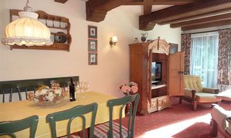 A cozy living area with a yellow dining table and chairs. The decor includes wooden ceiling beams and a harmonious color combination.