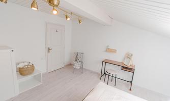 A bright bedroom with a modern, minimalist design. The walls are white, and there is a small desk as well as a cozy chair.