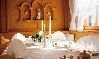A cozy dining area made of wood with a beautifully set table. On the table are candles and a flower arrangement.