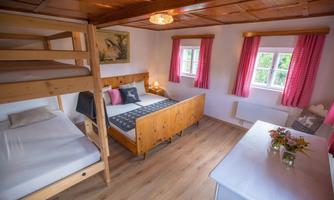 A cozy bedroom with a bunk bed and a double bed. The walls are painted light, and the colorful curtains create an inviting atmosphere.