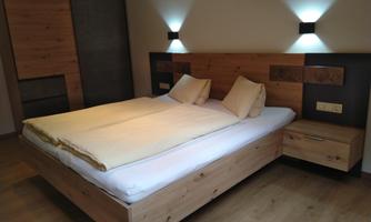 A modern bedroom with a wood bed and two pillows. The soft lighting creates a cozy atmosphere.
