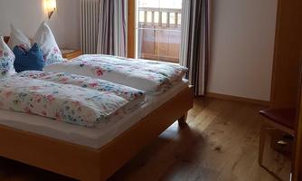 A cozy bedroom with a double bed and blue pillows. Large windows provide plenty of daylight and a beautiful view.