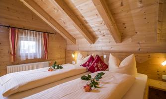A cozy mountain cabin with two single beds and a wooden ceiling. Decorations made of flowers and cushions create an inviting atmosphere.