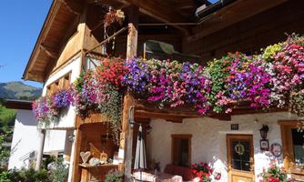 A charming rustic house with blooming balcony boxes full of colorful flowers. The clear blue sky and the mountain landscape in the background create an inviting atmosphere.