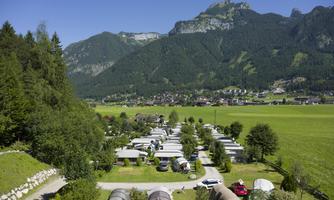An idyllic landscape with a campsite in the mountains. Green meadows and numerous RVs surrounded by impressive peaks.