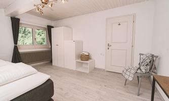 A bright room with a window and a view of the greenery. There is a bed, a wardrobe, and a chair in a modern, minimalist style.