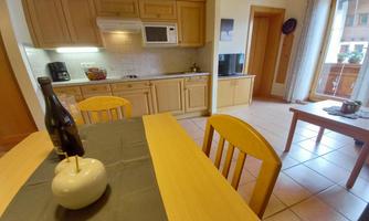 A bright kitchen with wooden cabinets and a dining table. On the table, there is a bottle of wine and a small decoration.