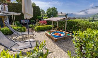 A cozy garden with two loungers and a sandbox. In the background, there are green bushes and a blue sky.