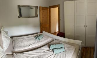 A cozy bedroom with two beds and a large wardrobe. The walls are light, and there is a mirror above the beds.