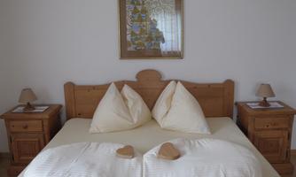 A cozy bedroom with a large bed and two heart-shaped pillows. The wooden nightstands and soft lighting create a warm atmosphere.