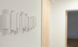 A wall with several white devices is visible. The background shows an open space with a wooden door frame.
