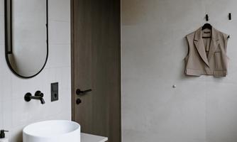 A modern bathroom with an elegant washbasin on a wooden cabinet. A mirror and a vest are hanging on the wall.