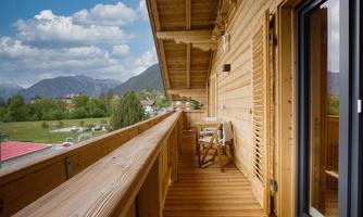 A beautiful wooden balcony overlooking green meadows and mountains. The clouds are blue and the sky is clear.