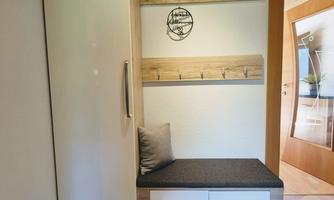 A modern entrance area with a white cabinet and a bench. Hooks for jackets and a decorative wall panel hang on the wall.