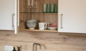 A modern kitchen with wooden walls and a sink. The upper cabinet is visible and contains dishes and glasses.