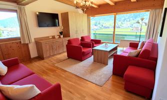 A modern living room with red armchairs and a wooden coffee table. Large windows offer a view of the green landscape.